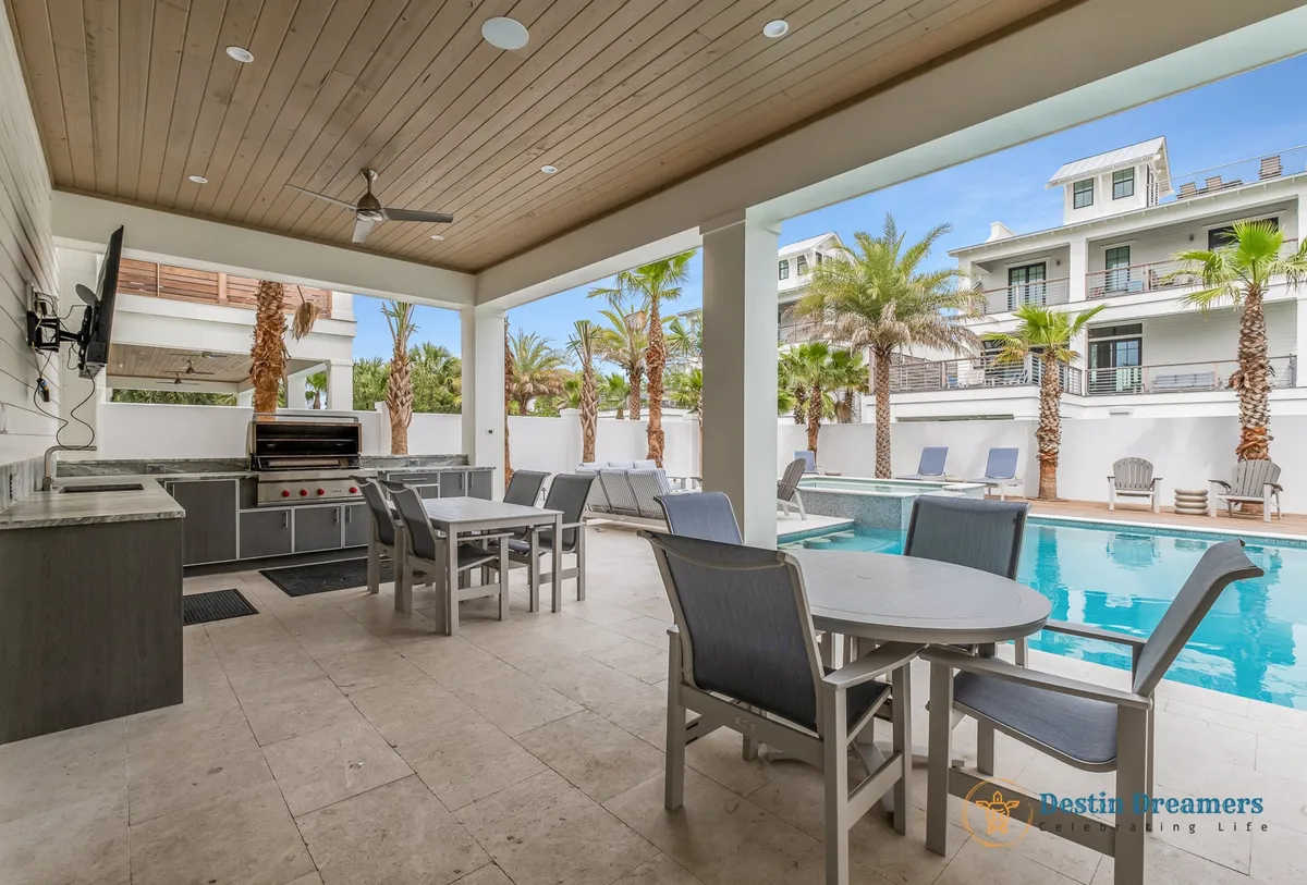 A lively outdoor gathering area featuring a grilling station, sparkling swimming pool, dining area, and lush palm trees. This space is designed for socializing, with plenty of seating for group barbecues or poolside meals, all set in a vibrant, welcoming atmosphere.