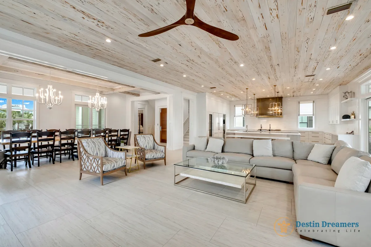 An expansive interior combining a large sectional sofa, a generous dining table with chairs, and a modern kitchen island in one open-concept space. Chandelier lighting creates an inviting mood, and the layout lends itself to family dinners, entertaining, and relaxing together.