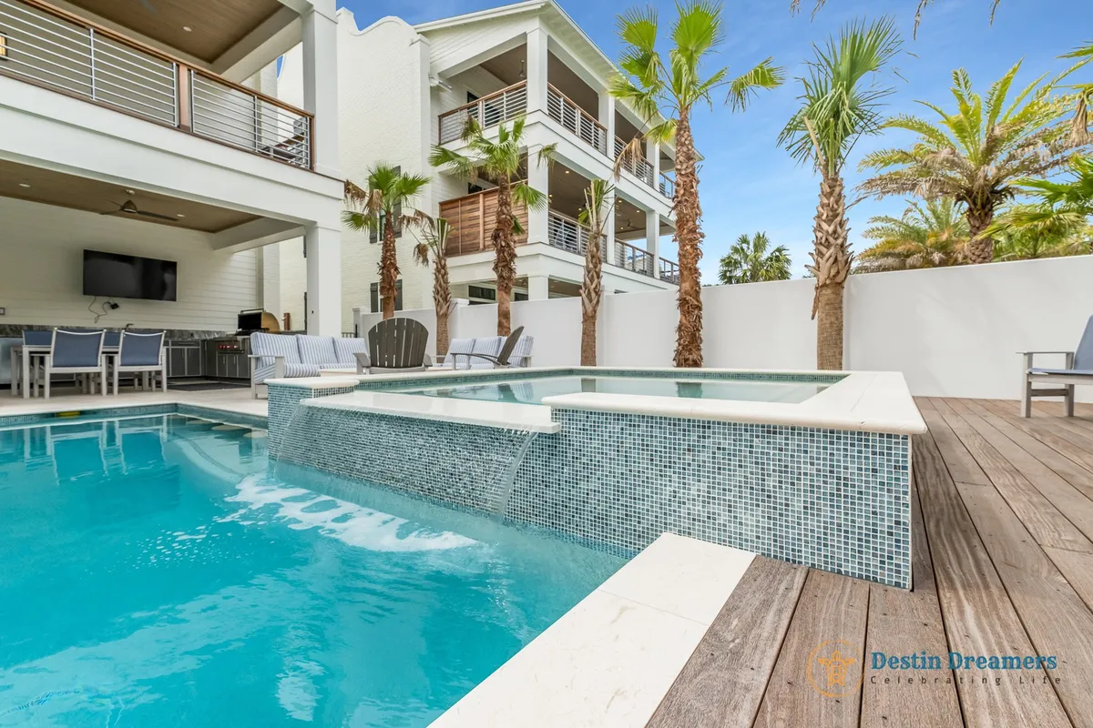 A stunning exterior scene featuring a shimmering swimming pool with an adjacent jacuzzi, surrounded by elegant palm trees and a stylish outdoor dining area. The deck captures the soft glow of sunset, making the area feel both exclusive and resort-like. There is ample space for lounging, swimming, and enjoying group activities.