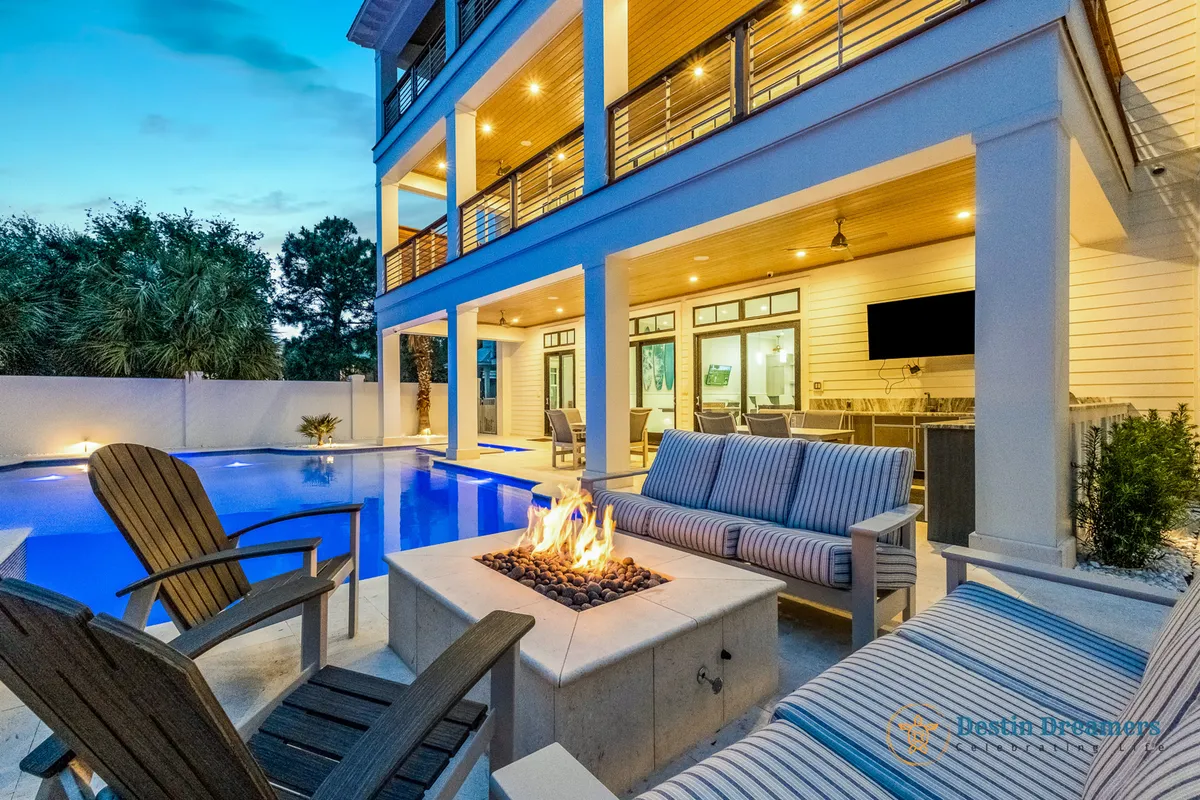 This exterior image features a vibrant backyard scene with a swimming pool, fire pit, outdoor seating, and ambient lighting, all set against a sunset sky. The spacious patio area provides ample room for relaxation and group gatherings.