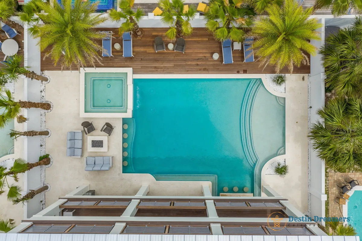 An inviting exterior shot of the private heated pool with swim-up bar stools, an outdoor seating area with a firepit, wooden deck with lounge chairs, and swaying palm trees. The atmosphere is tranquil and luxurious, ideal for both daytime play and evening relaxation.